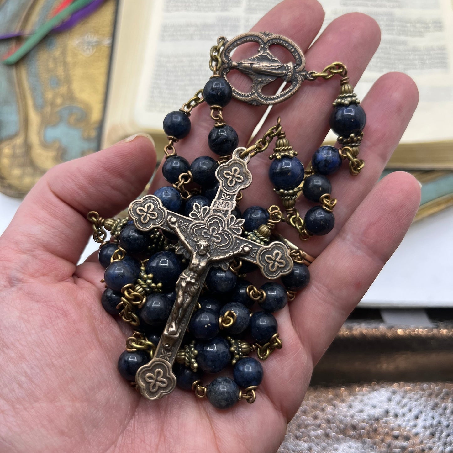 Hand holding blue Dumortierite rosary showing substantial size weight and solid bronze construction